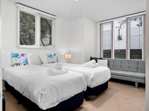 two beds in a bedroom with a couch and windows at Aspect 2 in Thredbo