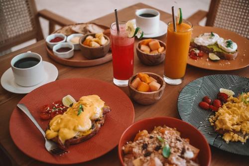 a wooden table with plates of breakfast food and drinks at Reset Lombok Hotel in Kuta Lombok