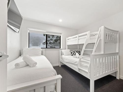 a white bedroom with two bunk beds and a window at Mowamba A1 in Thredbo