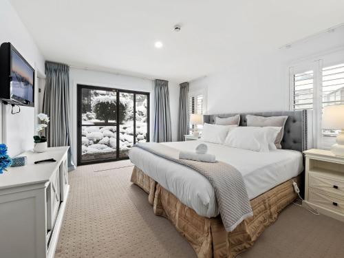 a white bedroom with a large bed and a television at Snowbound 1 in Thredbo