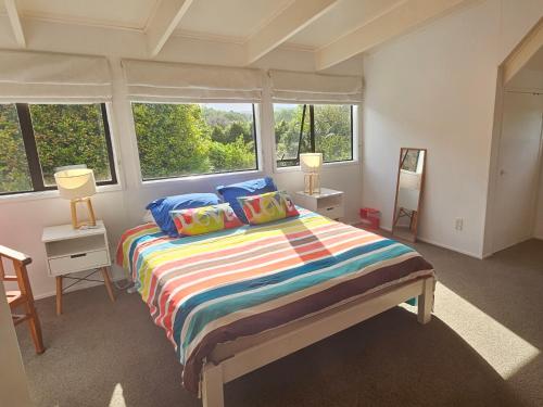 a bedroom with a bed with colorful sheets and windows at Forest Waters Bungalow in Haruru