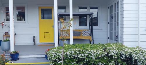 a yellow door on a white house with flowers at Morning Bloom Cottage Bed and Breakfast in Nelson