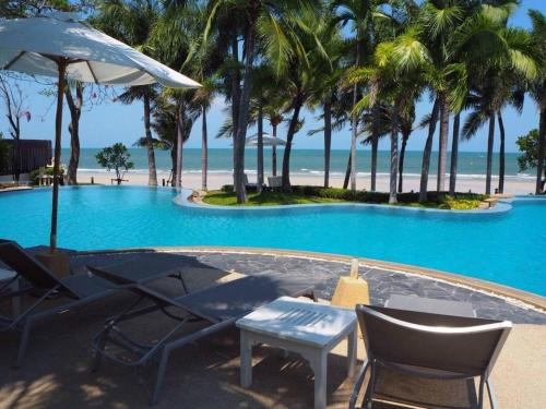 a pool with chairs and an umbrella and the beach at Baan Sanploen. Unit 244 in Hua Hin