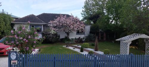 uma cerca azul em frente a uma casa com uma árvore florida em Morning Bloom Cottage Bed and Breakfast em Nelson