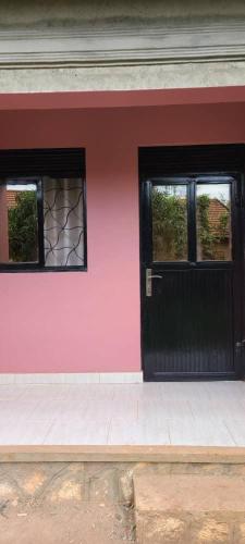 una casa rosa con una puerta negra y ventanas en Ronnie restate, en Jinja