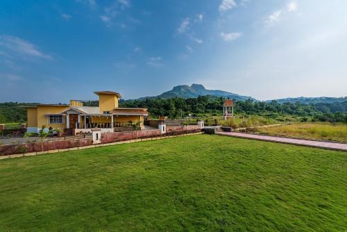 a house with a large green field in front of it at CosmicStays Rajgad Vista - Stay & play: adventure awaits in Welhe