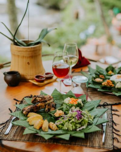a table with a plate of food and glasses of wine at Bambu Indah Resort in Ubud