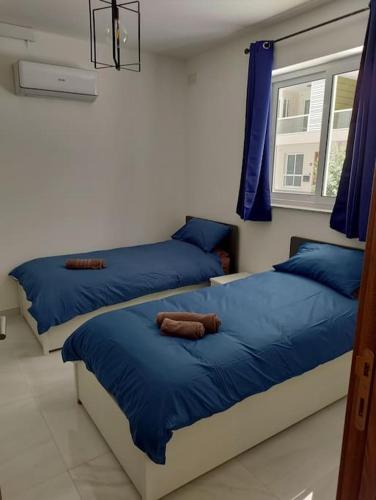1 Schlafzimmer mit 2 Betten mit blauer Bettwäsche und einem Fenster in der Unterkunft Modern Maisonette in Qawra in St Paul's Bay