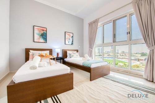 two beds in a room with a large window at Vivid 2BR at Canal Residences West Dubai Sports City by Deluxe Holiday Homes in Dubai