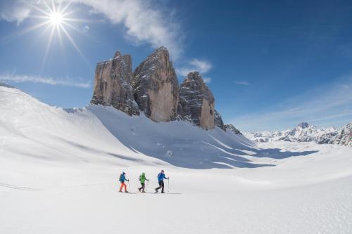 three people on skis in the snow in front of a mountain at Hotel Tre Cime Sesto - Sexten in Sesto