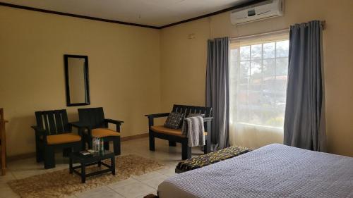 a bedroom with a bed and two chairs and a window at Quest in Lilongwe