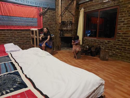 Due donne sedute in una stanza con un grande letto di A La Homestay a Hòa Bình