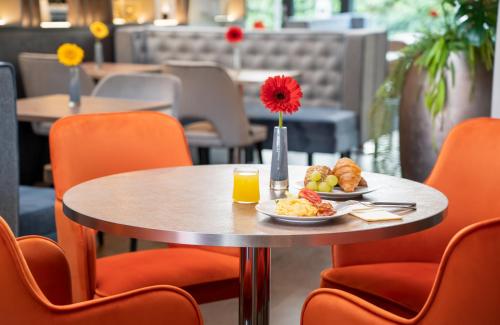 a table with a plate of food and orange chairs at Leonardo Hotel Vienna Hauptbahnhof in Vienna