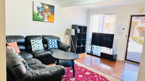 ein Wohnzimmer mit einem Ledersofa und einem Tisch in der Unterkunft Quiet family Townhouse in Wollongong CBD in Wollongong