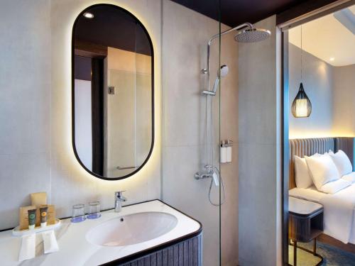 a bathroom with a sink and a mirror and a bed at Novotel Yogyakarta International Airport Kulon Progo in Yogyakarta