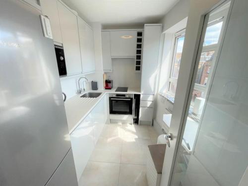 a white kitchen with white cabinets and a window at Large South Facing Studio Flat in London
