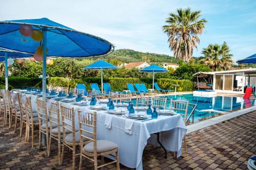 a long table with chairs and umbrellas next to a pool at Eleni Family Apartments in Sidari