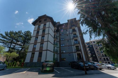 a tall building with cars parked in a parking lot at Apartman Zelenbor 4 Vila Zlatibor Luxury&Spa in Zlatibor