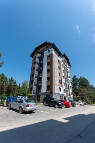 a tall building with cars parked in a parking lot at Apartman Zelenbor 4 Vila Zlatibor Luxury&Spa in Zlatibor