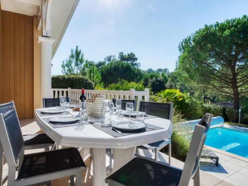 une table blanche et des chaises sur une terrasse avec piscine dans l'établissement Holiday Home Atlantic Green by Interhome, à Lacanau