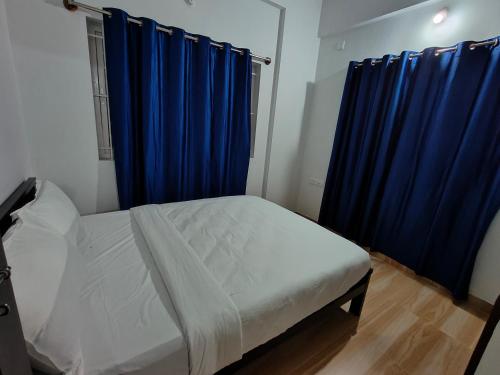 a bedroom with a bed with blue curtains and a window at Downtown Service Apartments in Mysore