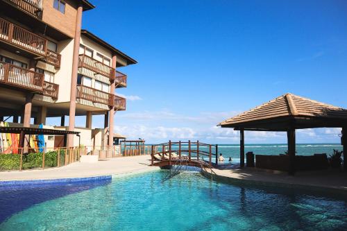 a swimming pool in front of a building with the ocean at APARTAMENTO 05 - PÉ NA AREIA - BARRA BALI - AL in Barra de São Miguel