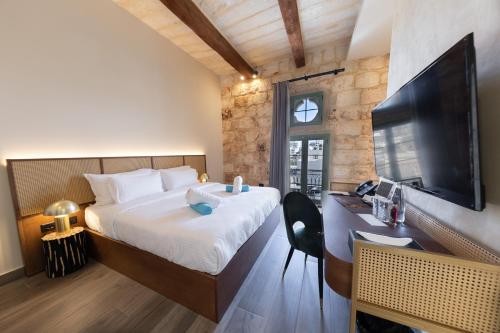 een slaapkamer met een groot bed, een bureau en een televisie bij DOMS Boutique Living in Mellieħa