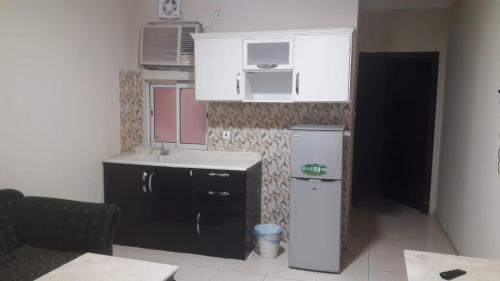 uma cozinha com armários brancos e um frigorífico preto em كوتاج المفروشة em Al Khobar