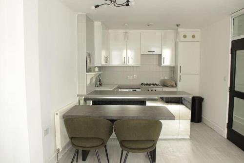 a kitchen with white cabinets and a counter with two chairs at 2 Bedroom Central London Apartment Modern and Stylish in London