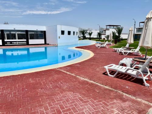 a swimming pool with chairs and umbrellas next to a building at Paracas Duplex 200 Metros - Sotavento 501 T 3 in Paracas
