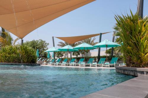 a swimming pool with blue chairs and umbrellas at Bay La Sun Hotel and Marina - KAEC in King Abdullah Economic City