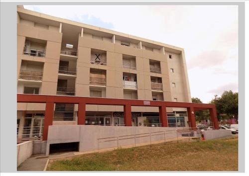 um grande edifício de apartamentos com um parque de estacionamento em frente em studio nimes costieres loggia parking em Nîmes