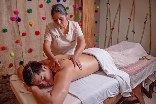 una mujer dándole un masaje a un hombre en una cama en Hotel Monasterio San Pedro, en Cusco
