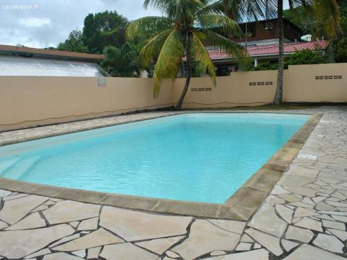 a blue swimming pool with a palm tree and a building at CoCoKreyol - " ARUBA" in Les Trois-Îlets