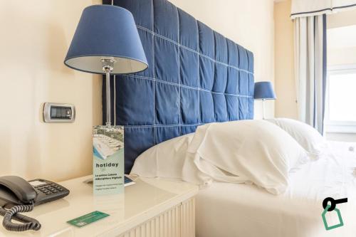 a bed with a blue headboard and a phone on a desk at HOTIDAY Room Collection - Livorno Mascagni in Livorno