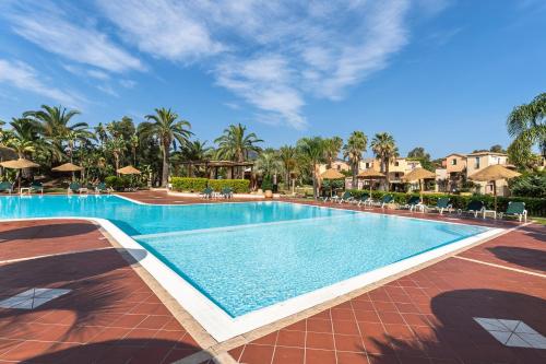 a swimming pool at a resort with palm trees at ISA-Residence with swimming-pool in Santa Margherita di Pula, apartments with air conditioning and private outdoor space at only 250 m from the beach in Santa Margherita di Pula