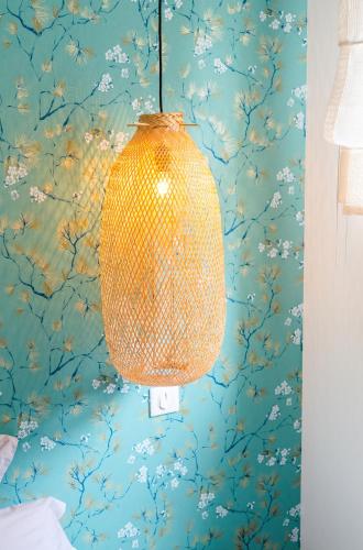 une lampe suspendue à un mur avec papier peint à fleurs dans l'établissement Escale à Saint-Gué, à Penmarcʼh