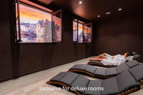 a woman laying in a bed in a room with two windows at Golden Tree Hotel in Bruges