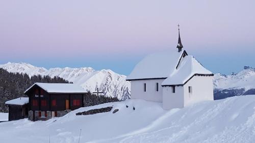 a church in the snow with mountains in the background at Imhof Alpine B&B Apartments in Bettmeralp