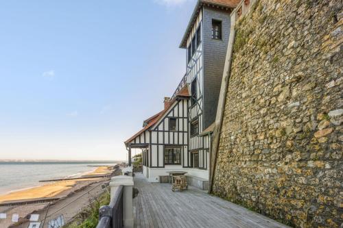 a building next to a stone wall next to the water at Charming house facing the sea in Villerville - Welkeys in Villerville