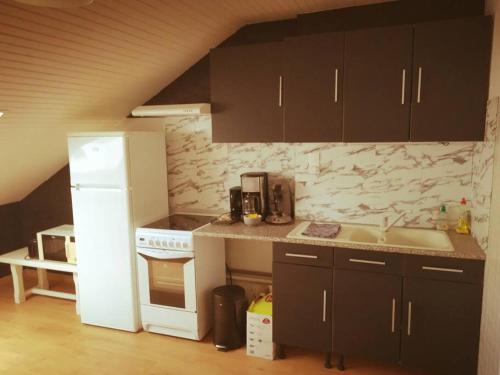 - une cuisine avec des armoires noires et un réfrigérateur blanc dans l'établissement Le Petit Loft Vosgien, à Cornimont