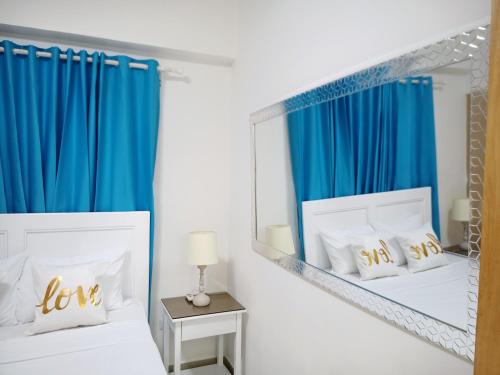 1 dormitorio con 2 camas, cortinas azules y espejo en Confortable apto. en Boca Chica en Boca Chica