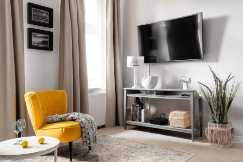 un salon avec une chaise jaune et une télévision dans l'établissement Sanhaus Apartments - Apartament LIDO - 300 m od plaży, à Sopot