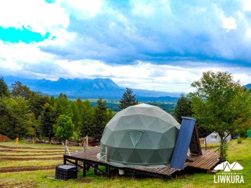 Tienda en una terraza de madera con una montaña al fondo en Agroglamping REFUGIO LIWKURA, en Caburgua