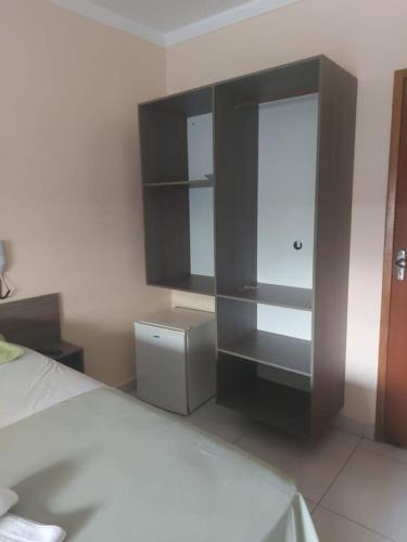 a bedroom with a bed and a dresser and a shelf at Hotel Pousada Aeroporto in Goiânia