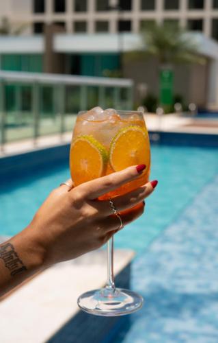 a woman holding a drink in front of a pool at Jade Hotel Brasília in Brasilia
