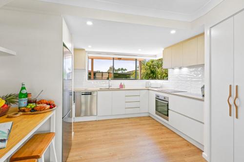a kitchen with white cabinets and a wooden floor at Sunrise Point Beach House by Experience Jervis Bay in Vincentia