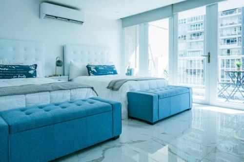 a white bedroom with two beds and a blue couch at Buena Vida Beach Studio Puerto Rico in San Juan