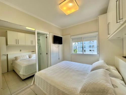 a white bedroom with a bed and a mirror at Apartamento de Luxo Capão da Canoa in Capão da Canoa