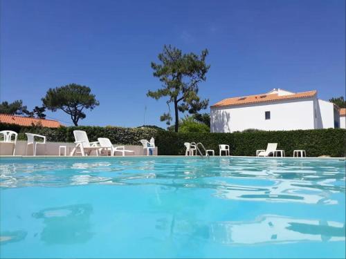 une piscine avec des chaises et une maison en arrière-plan dans l'établissement Appartement cosy avec piscine chauffée proche mer et centre – rénové et calme - FR-1-231-280, à Bretignolles-sur-Mer
